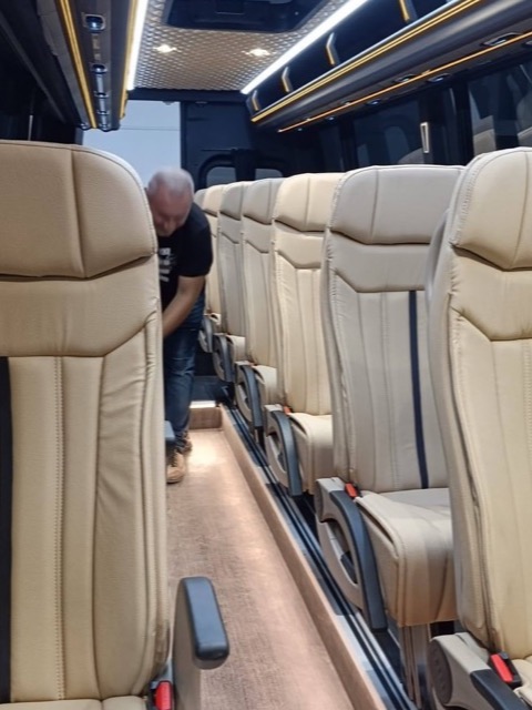 Intérieur du minibus : couloir central moquetté et rangées de sièges tapissés de similicuir